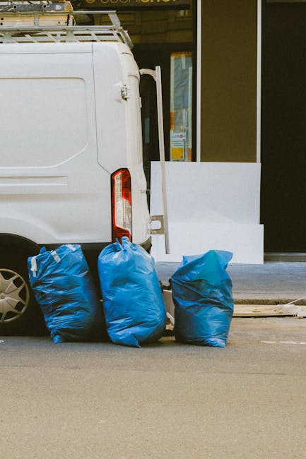 The image features the rear section of a white delivery van parked on a city street, with three large blue rubbish bags resting against the back wheel on the pavement. The bags are made of durable pla
