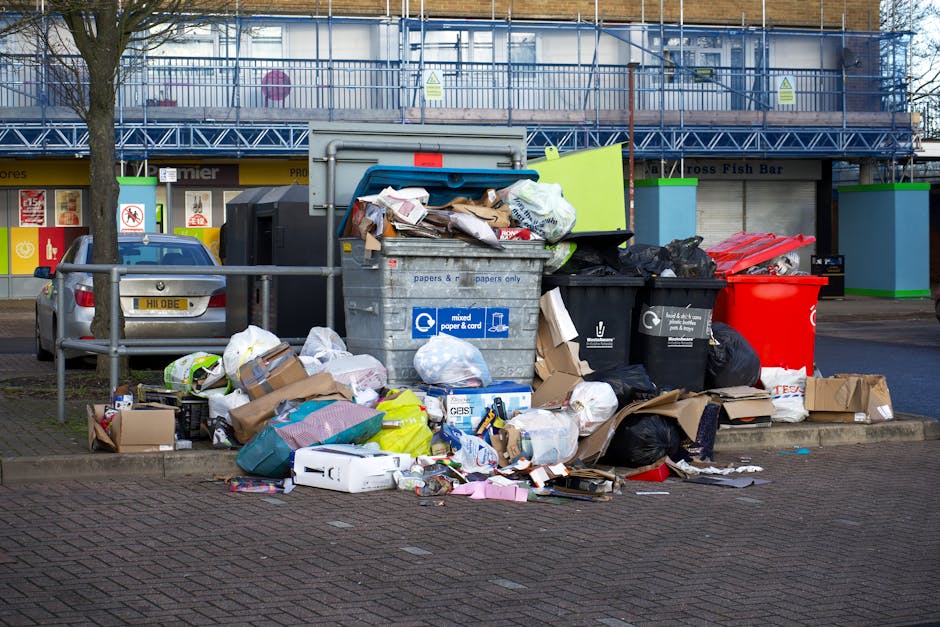 The image features the rear section of a white delivery van parked on a city street, with three large blue rubbish bags resting against the back wheel on the pavement. The bags are made of durable pla