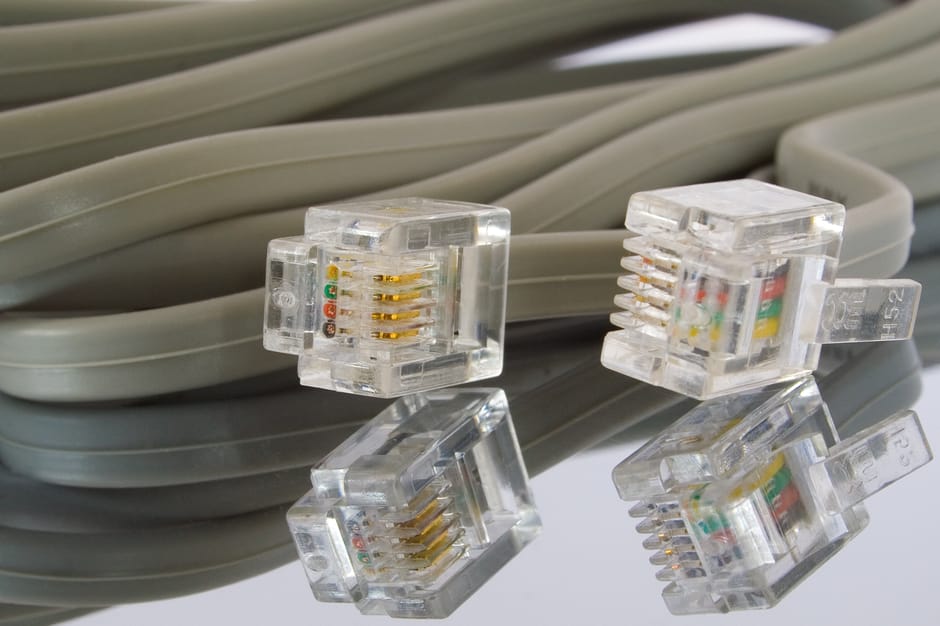 A close-up image of a neatly coiled grey Ethernet cable with four transparent RJ45 connectors resting on top. The connectors reveal the gold-plated contacts and multicolored wiring inside, indicating